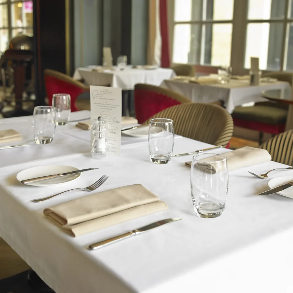 Salle de restaurant dressée, nappes blanches et serviettes beiges